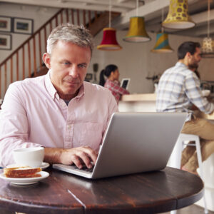 middle aged man in a coffee shop working at the supplemental real estate exam prep on his laptop